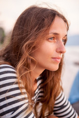 Portrait of a beautiful red-haired girl in T-shirt near the sea at the sunset. Pensive and happy girl. Relaxing near ocean. pretty girl