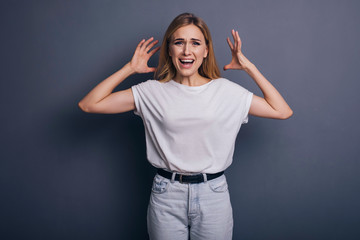 Caucasian woman in neutral casual outfit standing on a neutral grey background. Portrait with emotions: angry, pain, sickness and despair