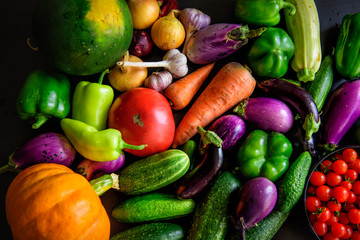 Harvest or Thanksgiving background with autumn vegetables on dark table. Seasonal ingredients for cooking: pumpkin, onions, carrots, eggplant, tomatoes, paprika, garlic, cucumbers. Top view, close-up.