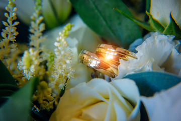 Fototapeta na wymiar Gold rings on a bridal bouquet, close-up. Shiny wedding rings among white flowers in bright light.