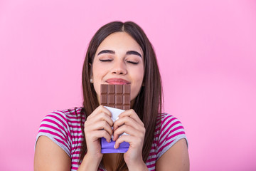 Lovely smiling teenage girl eating chocolate. Image of happy cute young woman standing isolated over pink background eating chocolate.