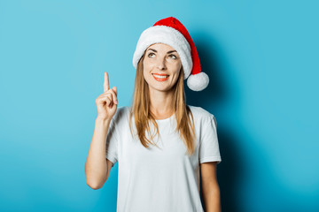 Young woman in Santa Claus hat with a mysterious face on a blue background. Concept idea for new year and christmas