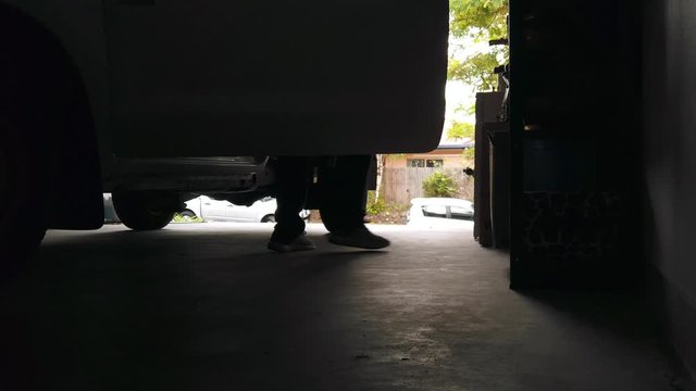 Silhouette Of A Man In Long Pants Exiting A Ute Suv In A Garage Carport Lit Behind From The Open Door