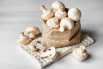 Mushrooms champignons in paper bag on a white wooden table. Place for text or advertising