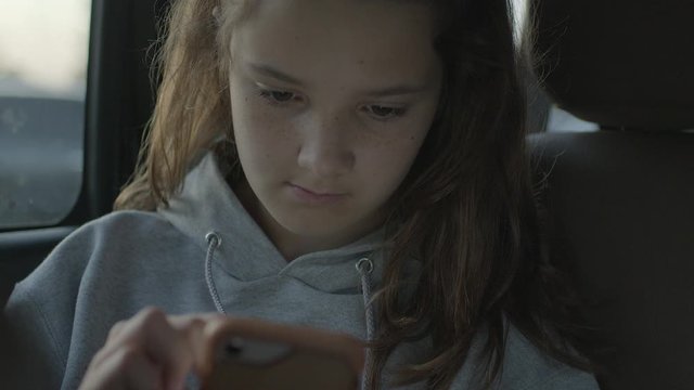 Teenage girl in the backseat of car on her smart phone