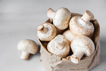Mushrooms champignons in paper bag on a white wooden table. Close up. Place for text or advertising