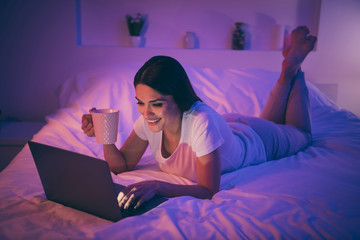 Nice attractive lovely cheerful cheery girl lying on bed using laptop chatting with boyfriend enjoying rest video contact call communicate online web cam drinking cacao at night room house flat