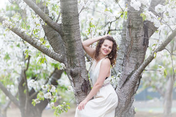 Naklejka na ściany i meble A portrait of beautiful young Caucasian woman with curly dark hair in blossoming orchard