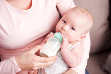 Obraz na płótnie Canvas Mother feeding baby with fresh milk on hands in room. Motherhood. Maternity.