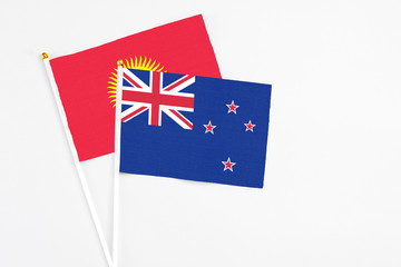 Fototapeta premium New Zealand and Kyrgyzstan stick flags on white background. High quality fabric, miniature national flag. Peaceful global concept.White floor for copy space.