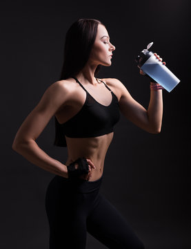 beautiful athletic woman in sportswear drinking protein cocktail over black