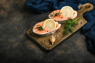 Fresh salmon steaks with herbs, lemon, rosemary and spices on a cutting board on a rustic background copy space.