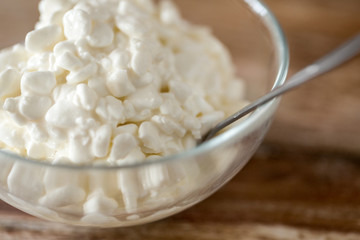 food and dairy products concept - close up of homemade cottage cheese in glass bowl on wooden table