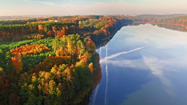 Forest and crystal clear lake with chemtrail reflection, aerial view