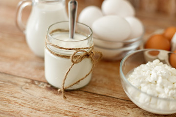 food and eating concept - close up of cottage cheese, jug of milk, homemade yogurt and chicken eggs on wooden table
