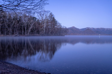 薄明の湖岸。静水に映る風景。屈斜路湖、北海道、日本。