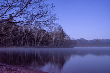 薄明の湖岸。静水に映る風景。屈斜路湖、北海道、日本。