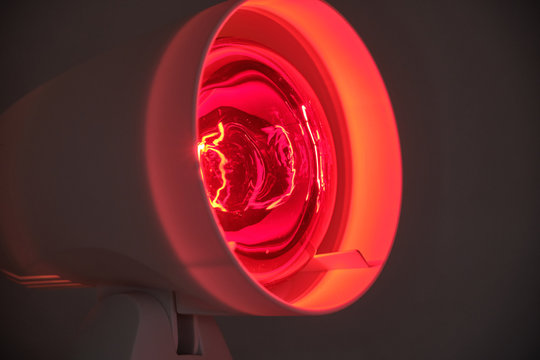 Close up of infrared lamp glowing in the dark with its warming red light to cure for example colds or tensions.