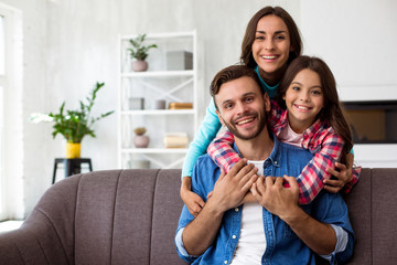 A power of three. Young handsome man is sitting on a couch and smiling while his wife and his...