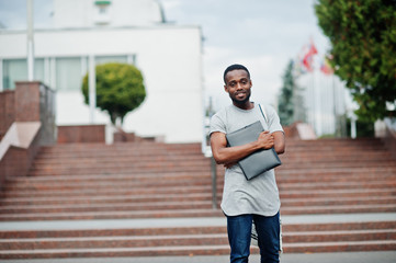 African student male posed with backpack and school items on yard of university, against flags of...
