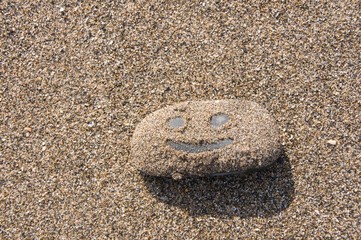Fototapeta na wymiar Smiling face pictured on sandy pebble 