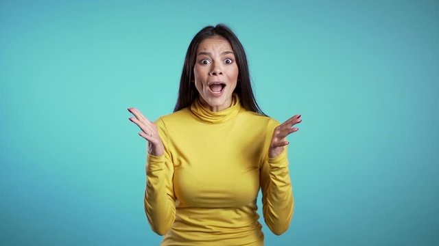 Portrait of cute mixed race girl shocked, saying WOW. Pretty latin woman smiling, jumping, pleasantly surprised to camera over blue background.