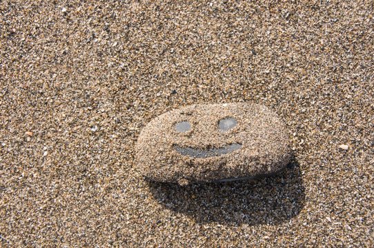 Smiling face pictured on sandy pebble 