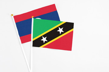 Saint Kitts And Nevis and Laos stick flags on white background. High quality fabric, miniature national flag. Peaceful global concept.White floor for copy space.