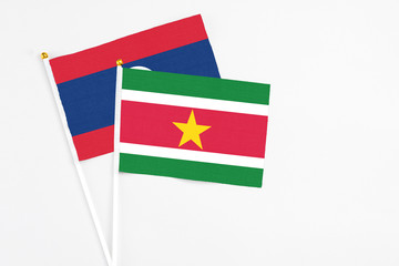 Obraz premium Suriname and Laos stick flags on white background. High quality fabric, miniature national flag. Peaceful global concept.White floor for copy space.