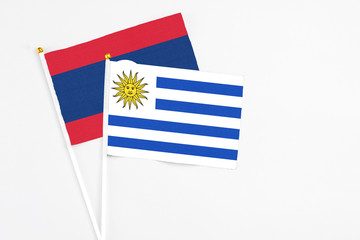 Uruguay and Laos stick flags on white background. High quality fabric, miniature national flag. Peaceful global concept.White floor for copy space.