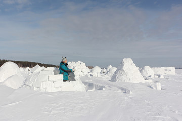 Happy woman in warm clothes building an igloo on a snow glade in the winter,  Novosibirsk, Russia