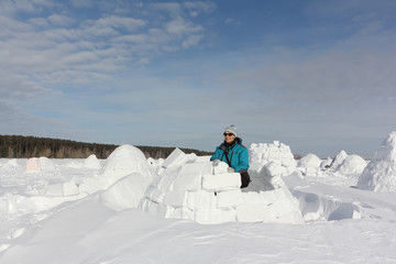 Happy woman in warm clothes building an igloo on a snow glade in the winter,  Novosibirsk, Russia