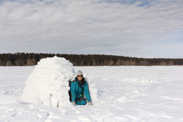 Happy woman in warm clothes sitting by an igloo in winter, Novosibirsk, Russia