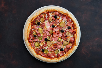 Top view of pizza with defferent kind of sausages, pickled cucumber, olives and onion