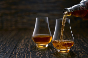 Man pouring whiskey in glasses  on rustic wooden table selective focus.