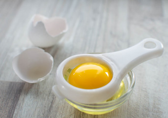 Separated egg white and yolk, egg shell on wooden table