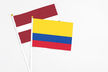 Colombia and Latvia stick flags on white background. High quality fabric, miniature national flag. Peaceful global concept.White floor for copy space.