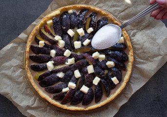 Homemade plum pie on the paper and dark background. Top view. Spoon with sugar.