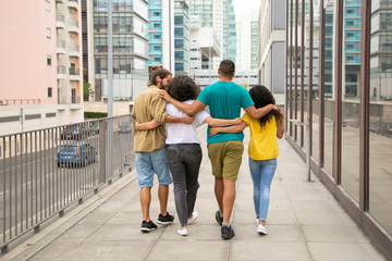 Obraz premium Rear view of friends walking outdoors. Back view of happy young multiethnic friends walking and talking together on street. Friendship concept