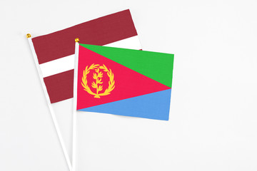 Eritrea and Latvia stick flags on white background. High quality fabric, miniature national flag. Peaceful global concept.White floor for copy space.