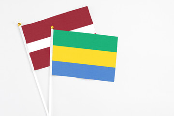 Gabon and Latvia stick flags on white background. High quality fabric, miniature national flag. Peaceful global concept.White floor for copy space.
