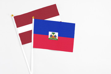 Haiti and Latvia stick flags on white background. High quality fabric, miniature national flag. Peaceful global concept.White floor for copy space.