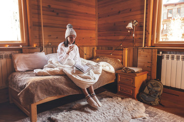 Girl relaxing and reading book in cozy log cabin in winter