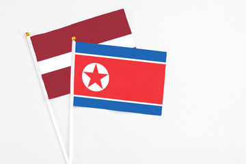 North Korea and Latvia stick flags on white background. High quality fabric, miniature national flag. Peaceful global concept.White floor for copy space.