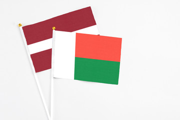 Madagascar and Latvia stick flags on white background. High quality fabric, miniature national flag. Peaceful global concept.White floor for copy space.