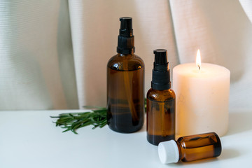 Rosemary essential oils in glass bottles with a candle on white background with drapery.