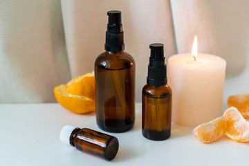 Aromatherapy essential oils in glass bottles with fresh citrus fruit and white candle on white drapery background.