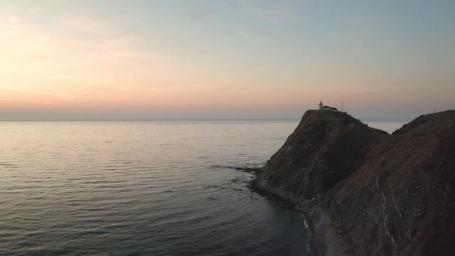Drone flight at sunrise over the lighthouse at Cape Emine, surrounded by turquoise green sea and mountain slopes - Black sea coast, Bulgaria.