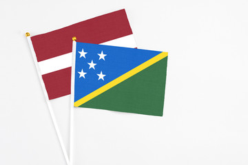 Solomon Islands and Latvia stick flags on white background. High quality fabric, miniature national flag. Peaceful global concept.White floor for copy space.