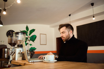 Businessman using laptop with tablet on wooden table in coffee shop with a cup of coffee.